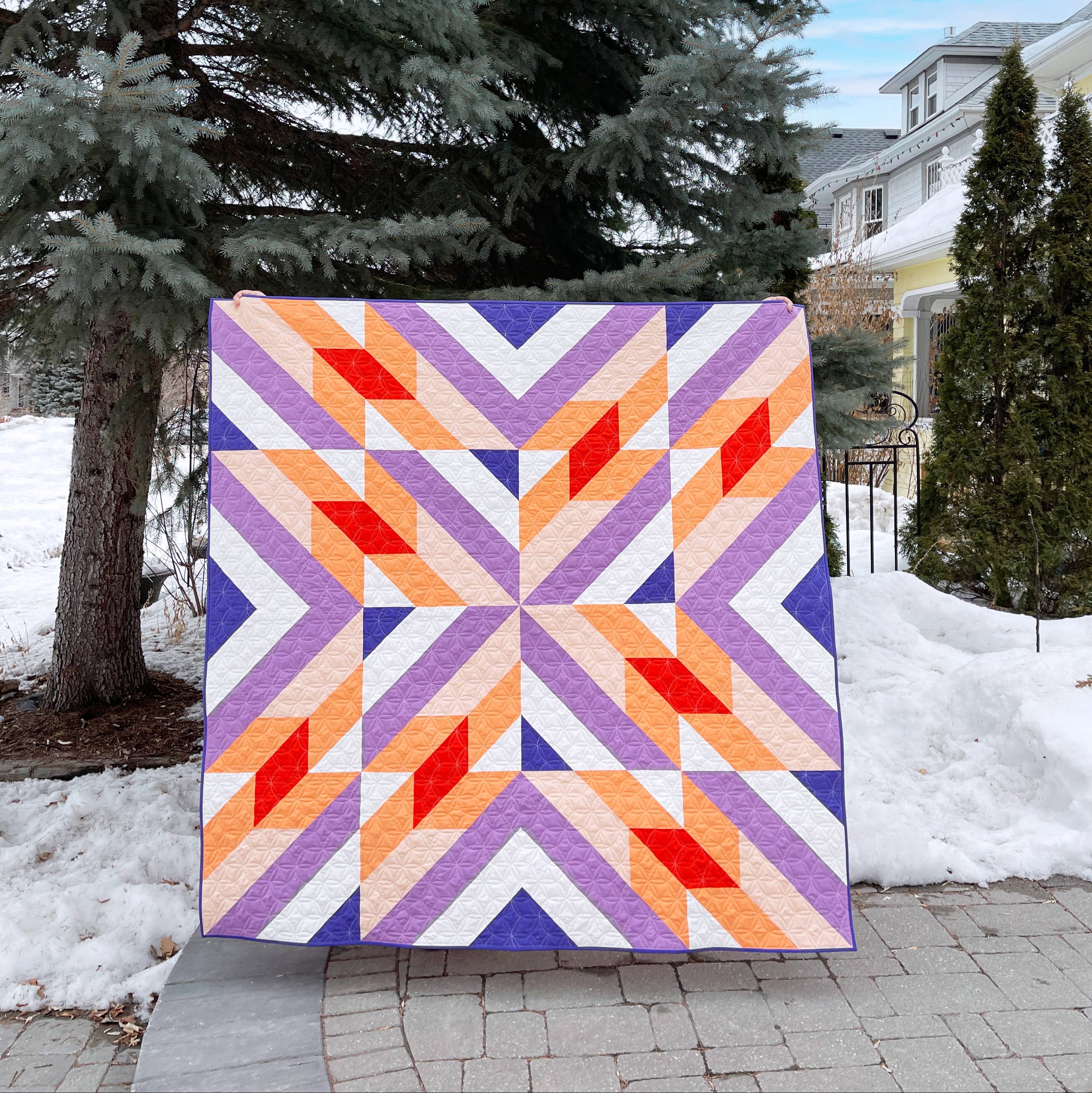 Colourful geometric quilt displayed outdoors with snow and trees in the background