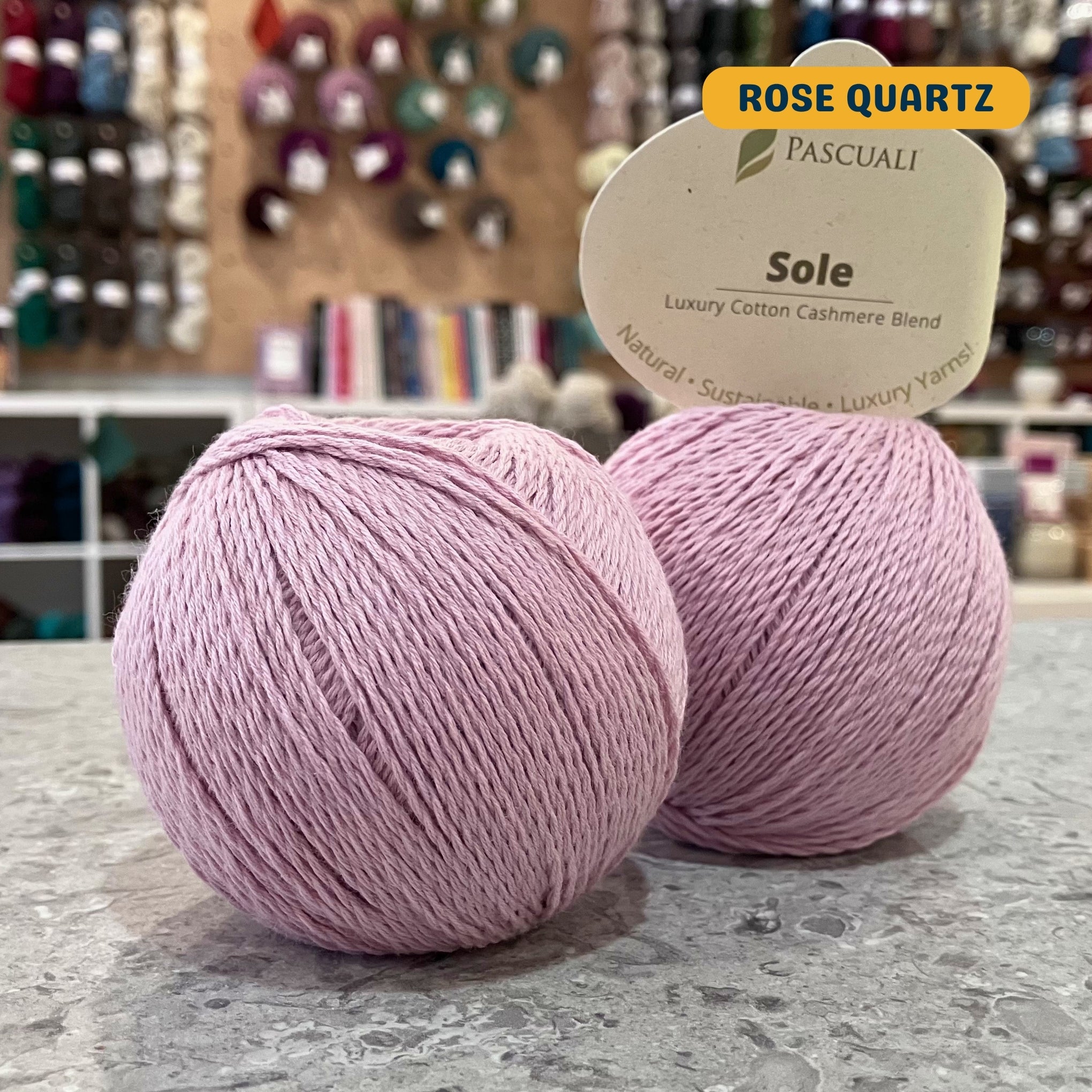 50g light pink (rose quartz) cotton & cashmere sport yarn, 'Pascuali Sole Luxury Cotton Cashmere Blend' label visible, craft shop background (blurred)