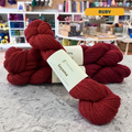50g red (ruby) baby llama & wool DK yarn, 'Pascuali Sayama Bolivian Llama and Virgin Wool Blend' label visible, craft shop background (blurred)