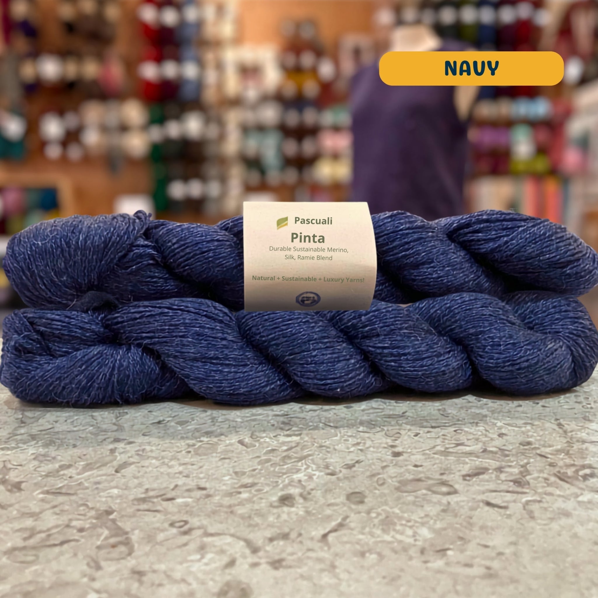 50g dark blue (navy) merino, silk, & ramie sock yarn, 'Pascuali Pinta Durable Organic Merino Silk Ramie Blend' label visible, craft shop background (blurred)