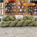 50g light green (pistachio) merino, silk, & ramie sock yarn, 'Pascuali Pinta Durable Organic Merino Silk Ramie Blend' label visible, craft shop background (blurred)