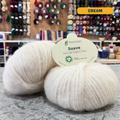 25g cream organic cotton sport yarn, 'Pascuali Suave Extra Light Organic Cotton' label visible, craft shop background (blurred)
