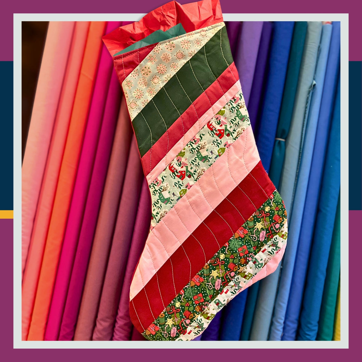Sample image for quilting workshop. Halifax, Nova Scotia.
A handmade quilted Christmas stocking with diagonal stripes of red, pink, green, and holiday fabrics, hanging in front of a colourful array of bolted quilting cotton fabrics.