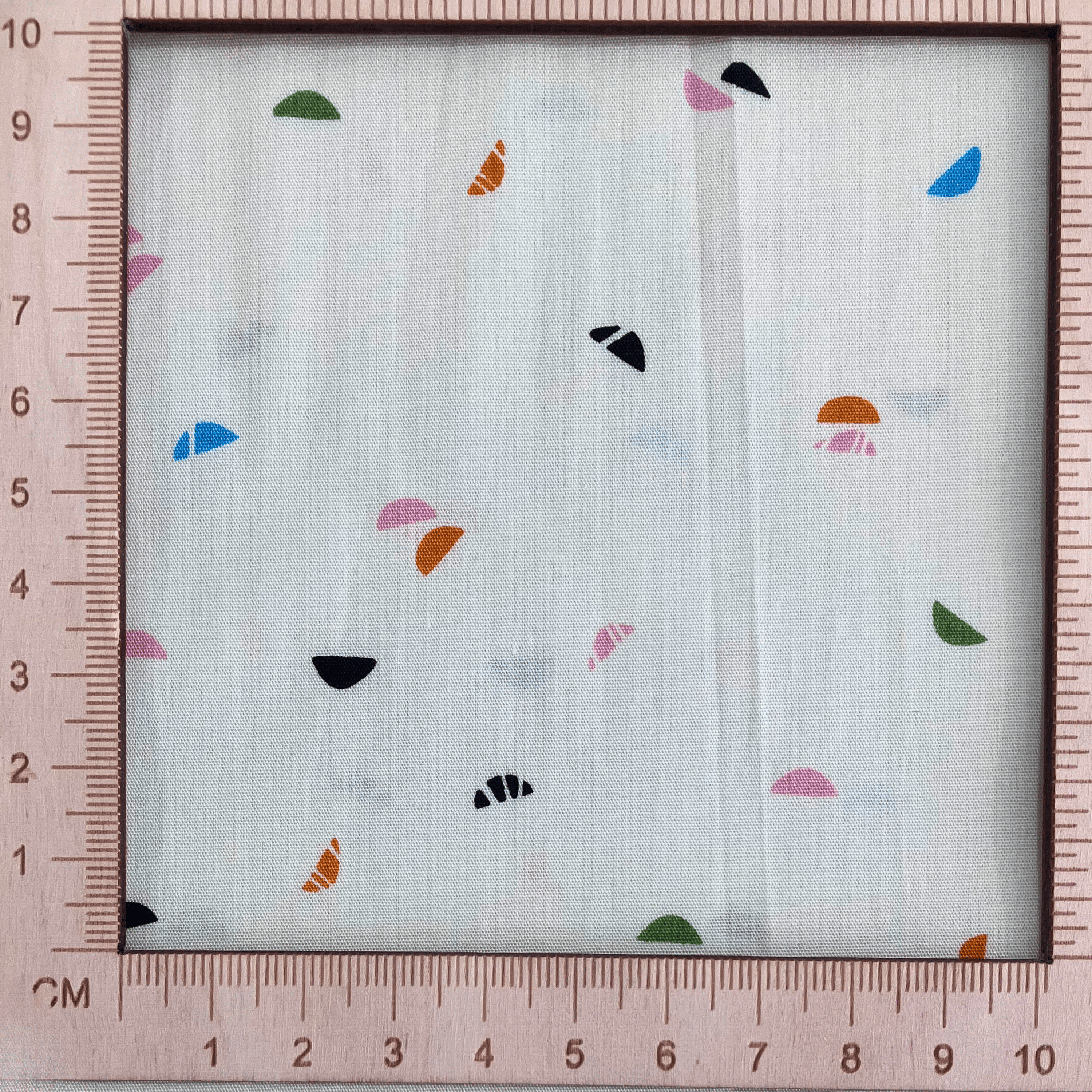 4"x4" scale — 100% cotton quilting fabric — light cream fabric with green, blue, pink, orange, and black crescent shapes. 44/45in width.