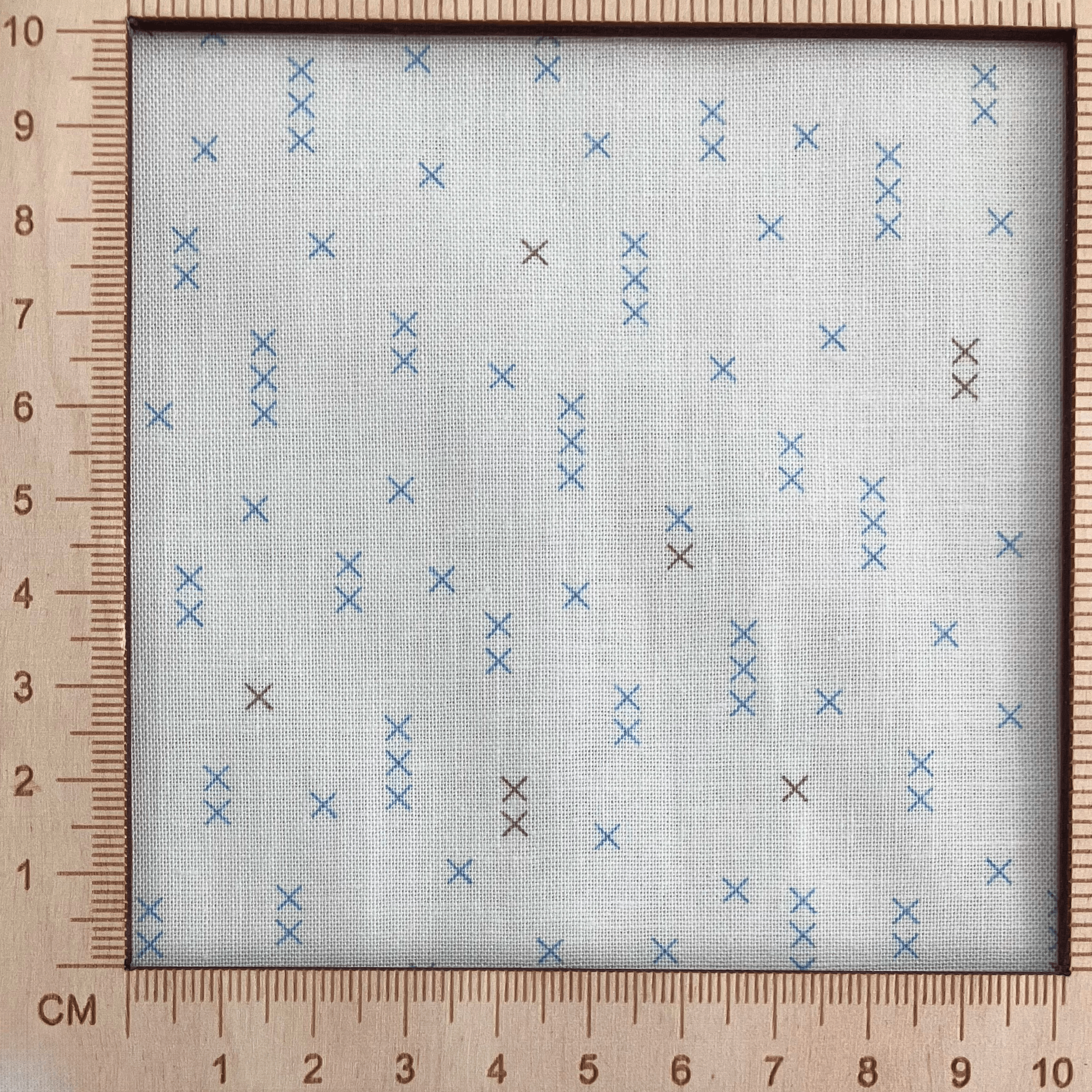 4"x4" scale — 100% cotton quilting fabric — light beige fabric with grey and blue x’s. 44/45in width.