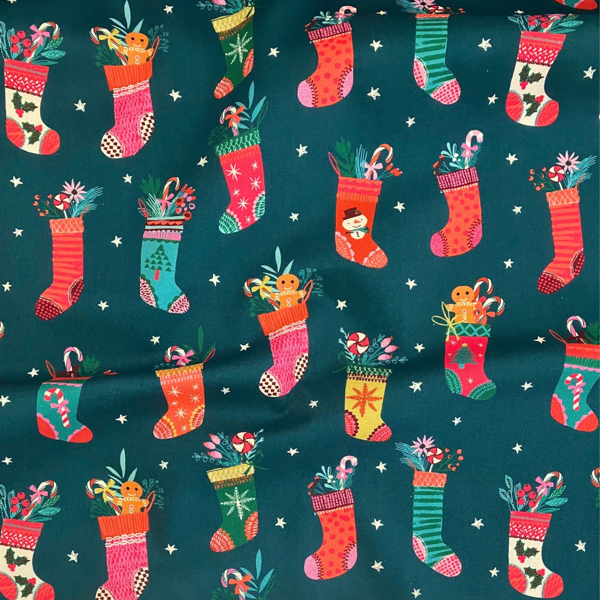Christmas Stockings quilting cotton — illustrated Christmas stockings stuffed with candy canes and gingerbread on a deep teal background with white stars. Dashwood Studio, 44/45″ wide.