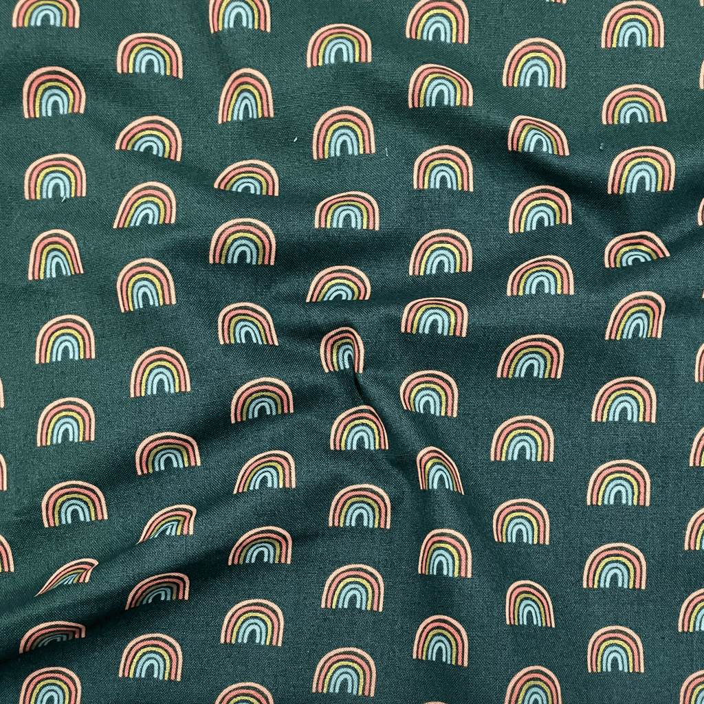 100% cotton quilting fabric — small rainbows on dark green. 43/44in width.
