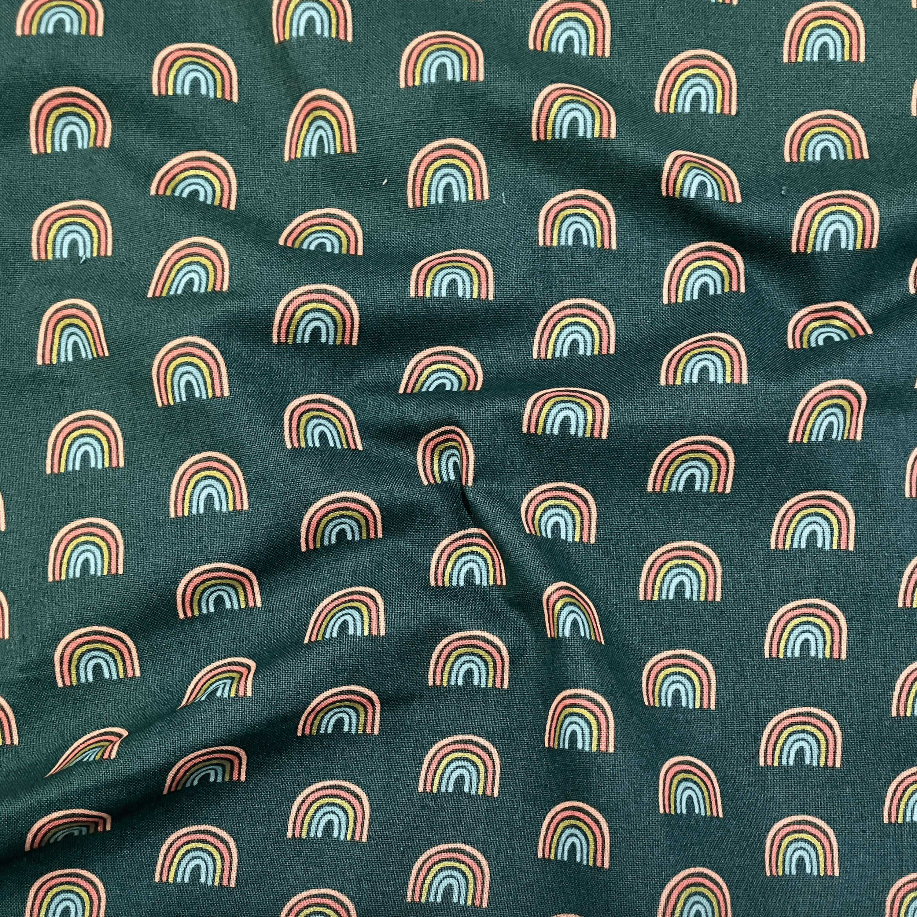 100% cotton quilting fabric — small rainbows on dark green. 43/44in width.