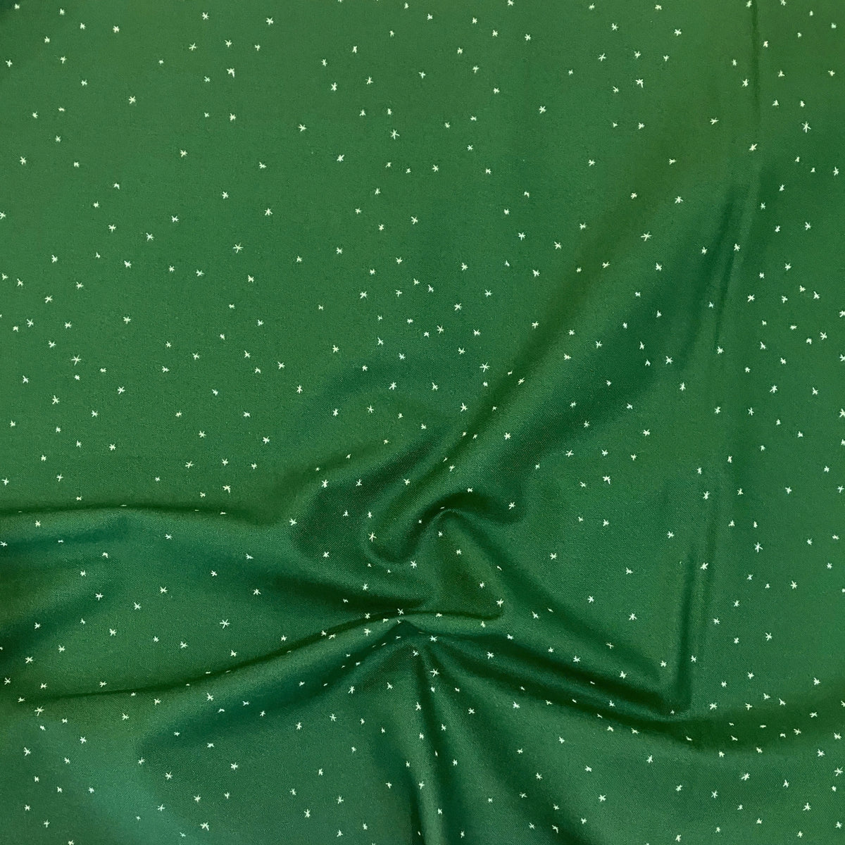 Flurries quilting cotton — scattered white snowflake stars on a rich forest green background. Phoebe Fabrics Wintry collection, 43/44″ wide. Canadian.
