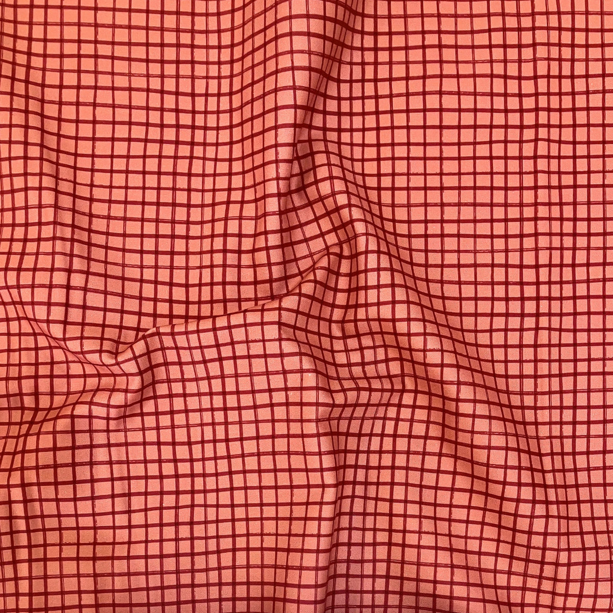 Plaid Sketch quilting cotton — hand-drawn grid check in deep cranberry on a warm salmon pink background. Phoebe Fabrics Wintry collection, 43/44″ wide. Canadian.