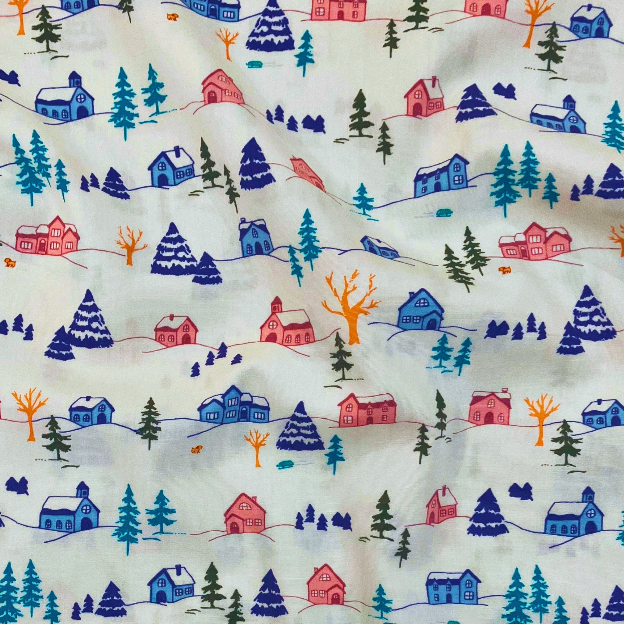 Winterful Town quilting cotton — illustrated winter village with snow-dusted houses, evergreen trees and woodland animals in cobalt, pink and teal on cream. Art Gallery Fabrics, 44/45″ wide.