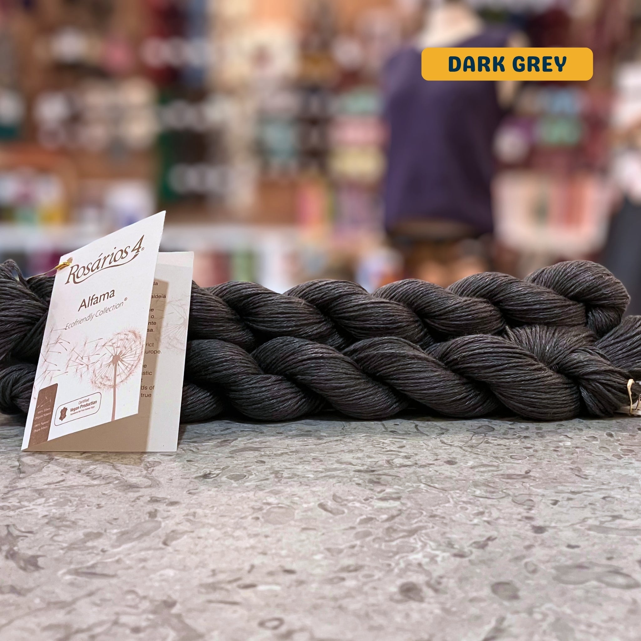 50g dark grey pure linen dk yarn, 'Rosários4 Alfama Ecofriendly Collection' label visible, craft shop background (blurred)