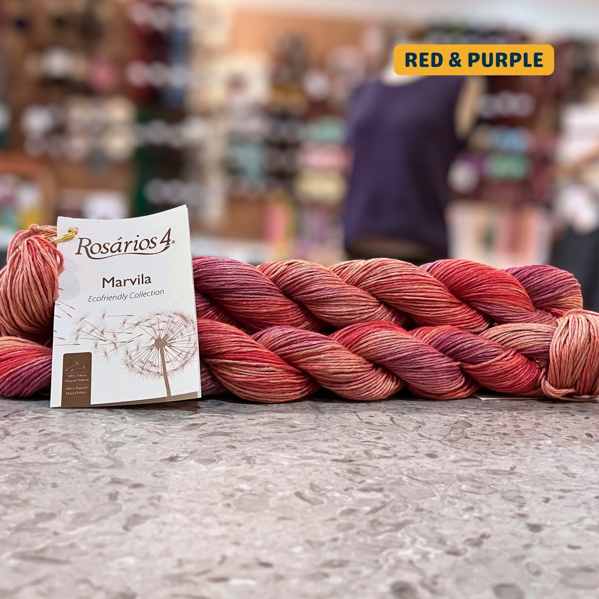 50g variegated red & purples pure linen dk yarn, 'Rosários4 Marvila Ecofriendly Collection' label visible, craft shop background (blurred)
