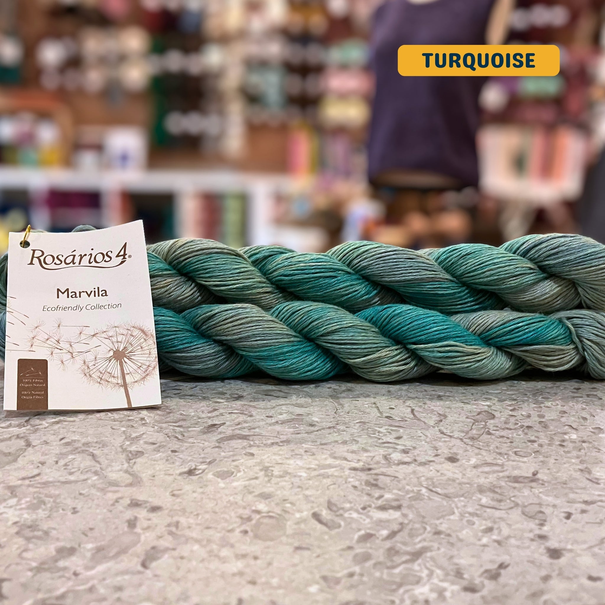 50g variegated blues & greens (turquoise) pure linen dk yarn, 'Rosários4 Marvila Ecofriendly Collection' label visible, craft shop background (blurred)