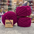 50g deep pink (sangria with friends) GRS-certified recycled wool worsted yarn, 'Spun Up reclaim recreate relove' label visible, craft shop background (blurred)