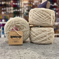 50g natural white (whispering willow) GRS-certified recycled wool worsted yarn, 'Spun Up reclaim recreate relove' label visible, craft shop background (blurred)