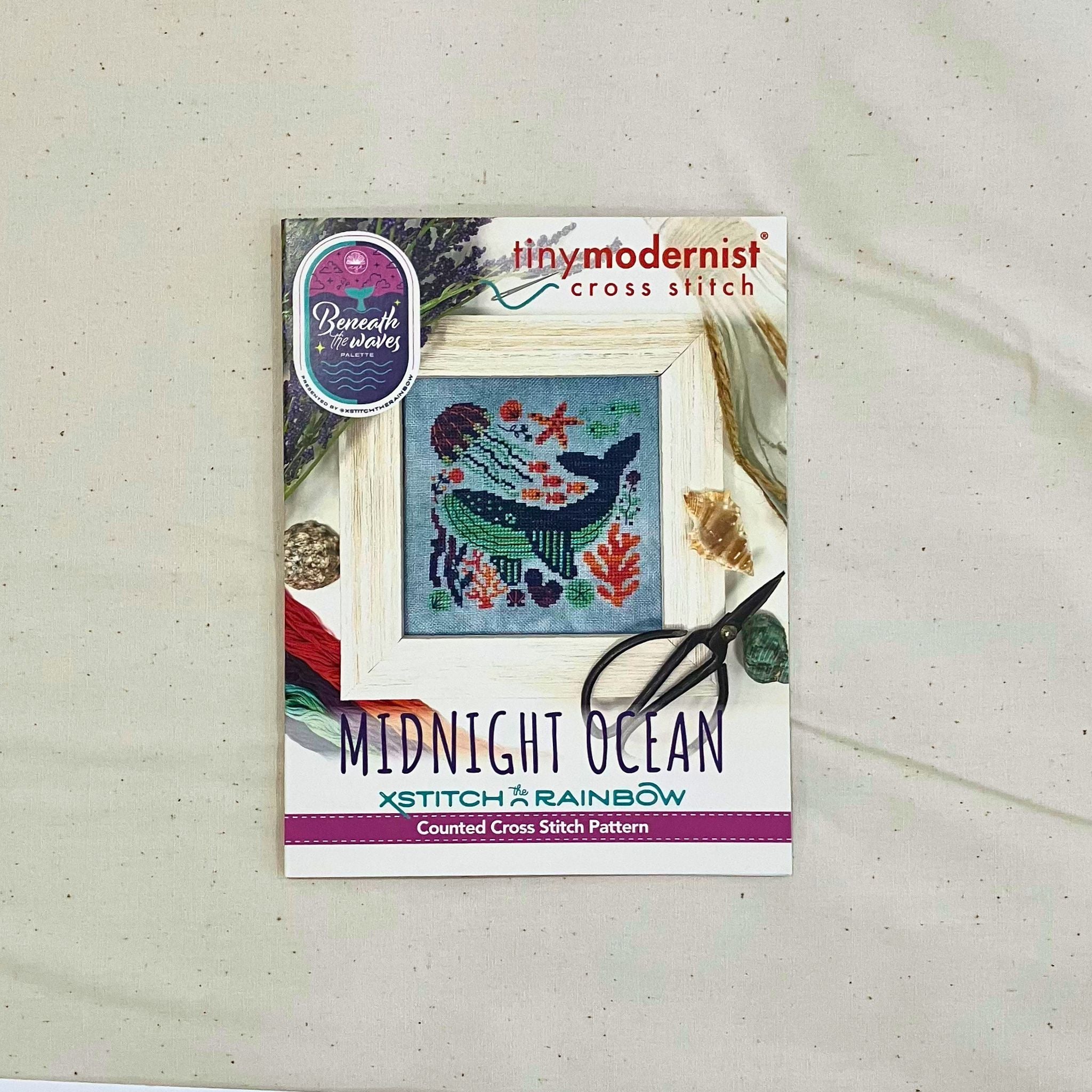 A counted cross stitch pattern card for 'Midnight Ocean' by Tiny Modernist Cross Stitch, featuring a finished sample of a whale, jellyfish, & coral.