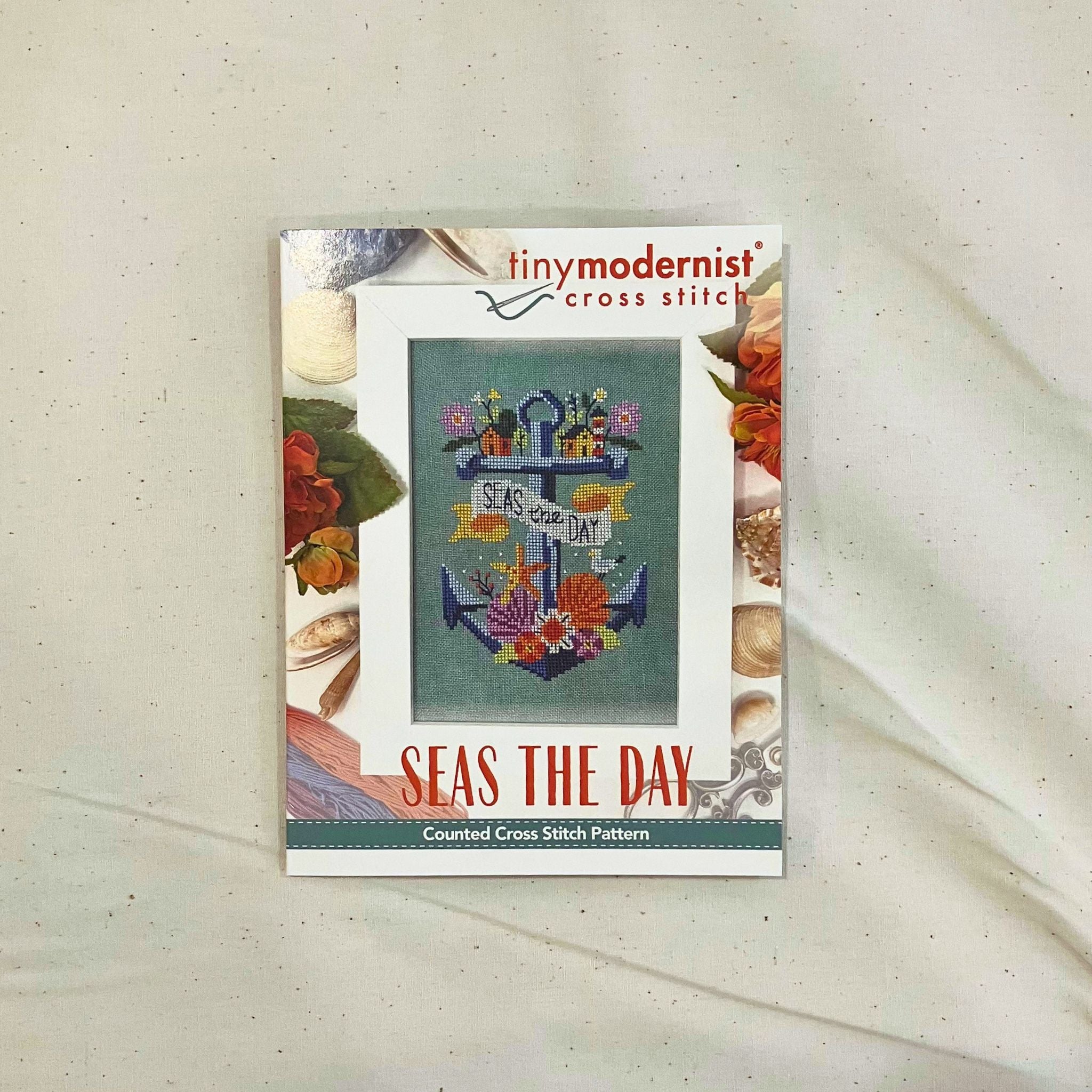 A counted cross stitch pattern card for 'Seas the Day' by Tiny Modernist Cross Stitch, featuring a finished sample of a anchor & sea shells.