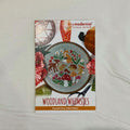 A counted cross stitch pattern card for 'Woodland Whimsies' by Tiny Modernist Cross Stitch, featuring a finished sample of a colourful cross-stitched woodland design with deer, mushrooms, flowers, and a fox.