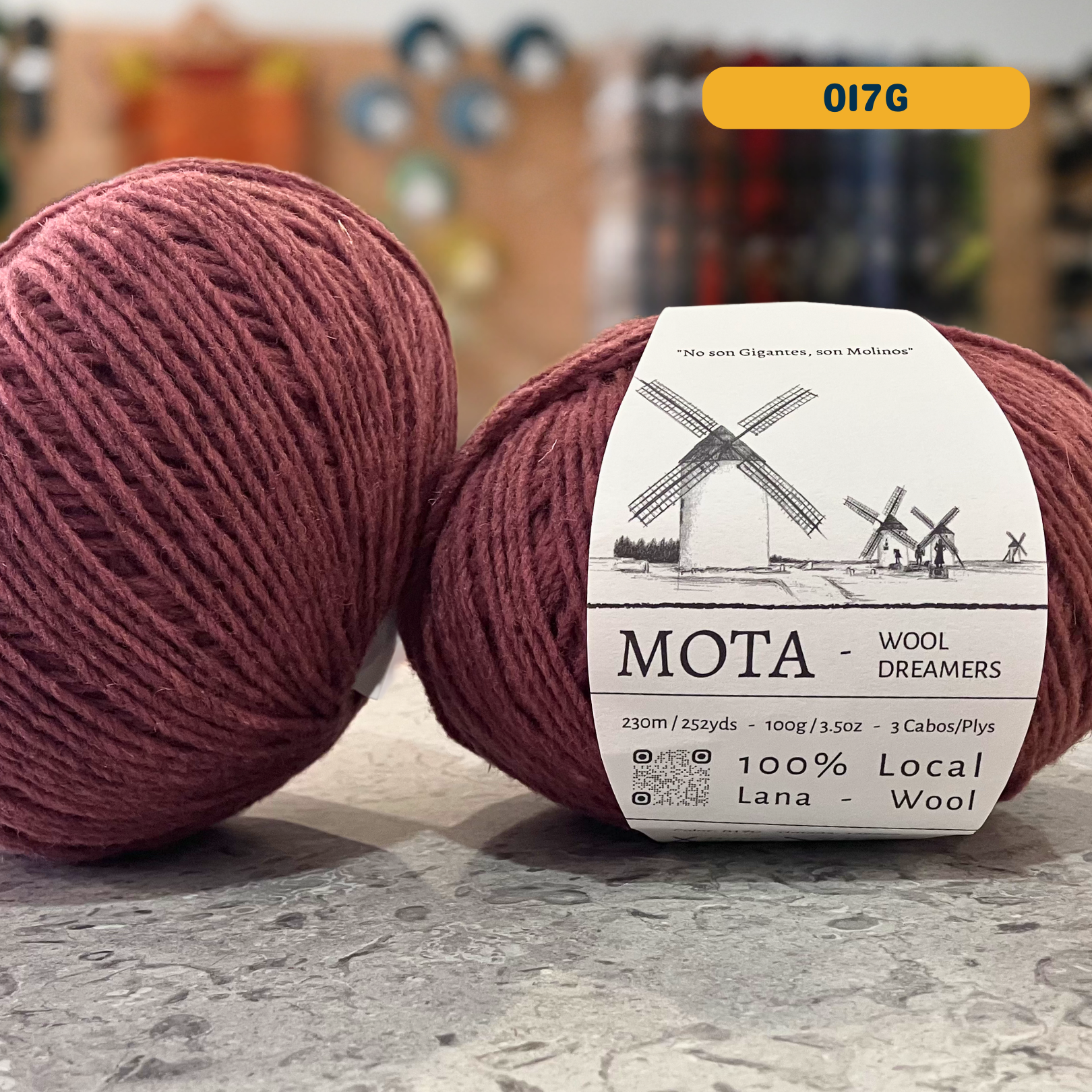 100g light maroon (017G) merino & manchega wool yarn, 'Mota Wooldreamers 100% Wool' label visible, craft shop background (blurred)