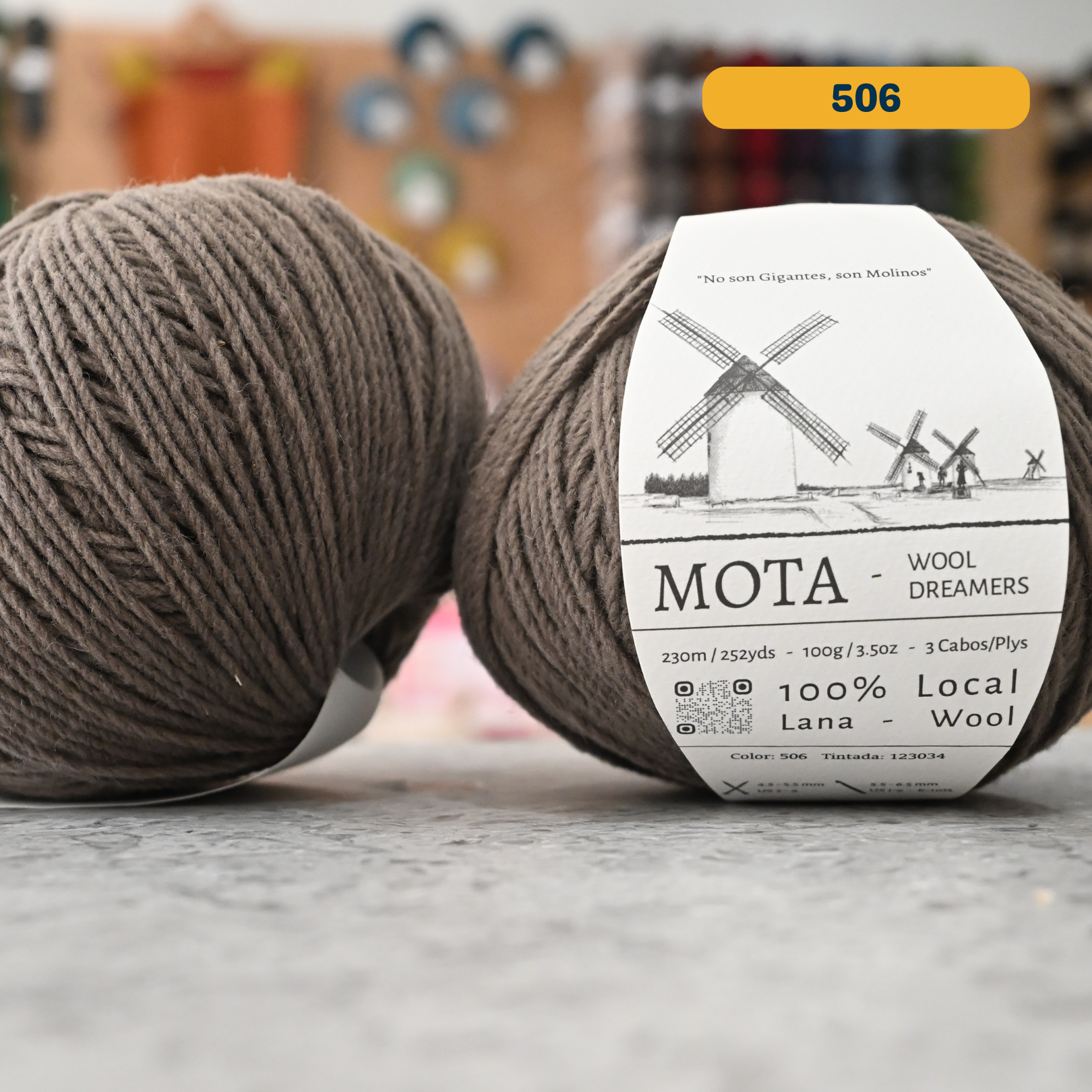 100g grey-brown (1526G) merino & manchega wool yarn, 'Mota Wooldreamers 100% Wool' label visible, craft shop background (blurred)
