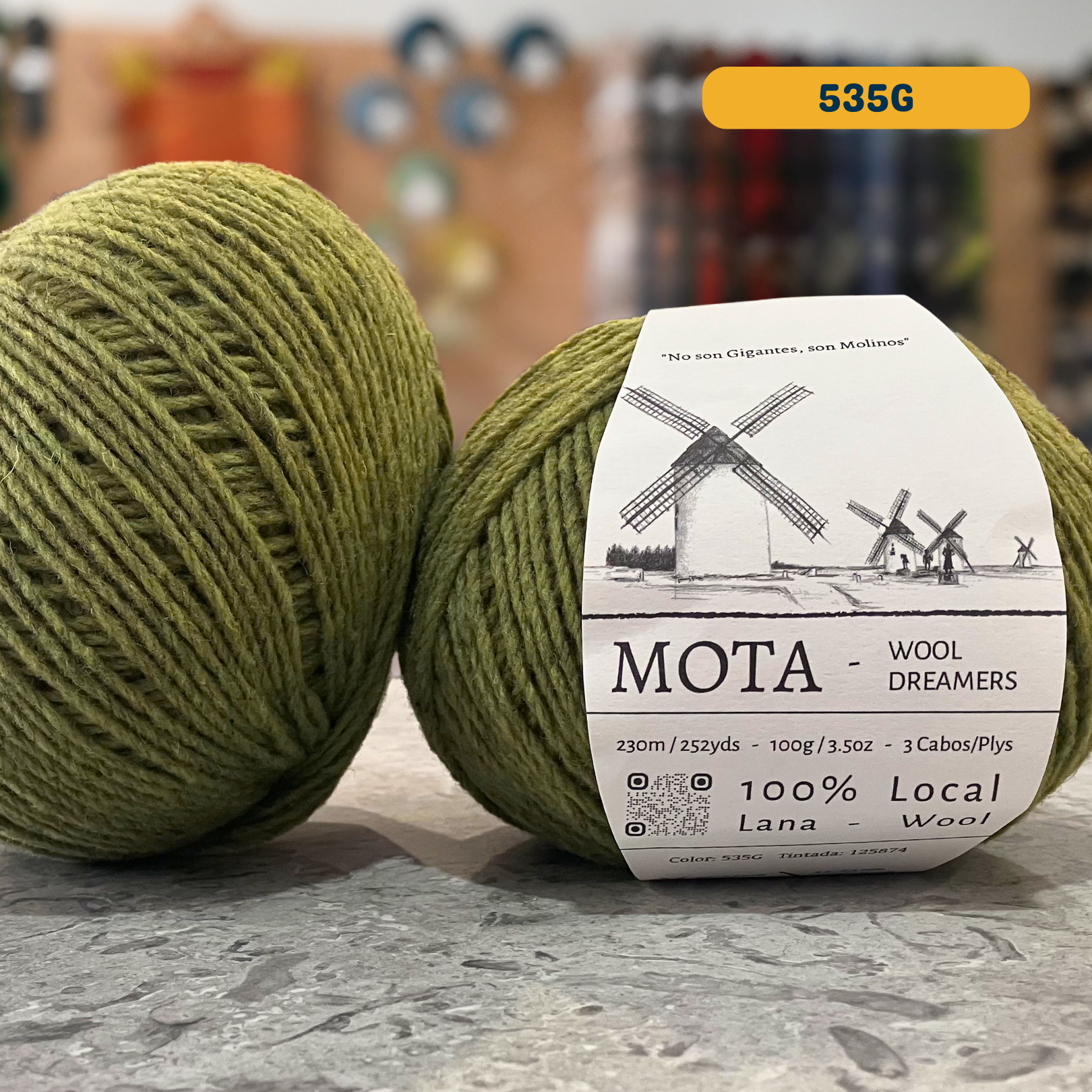 100g green (535G) merino & manchega wool yarn, 'Mota Wooldreamers 100% Wool' label visible, craft shop background (blurred)
