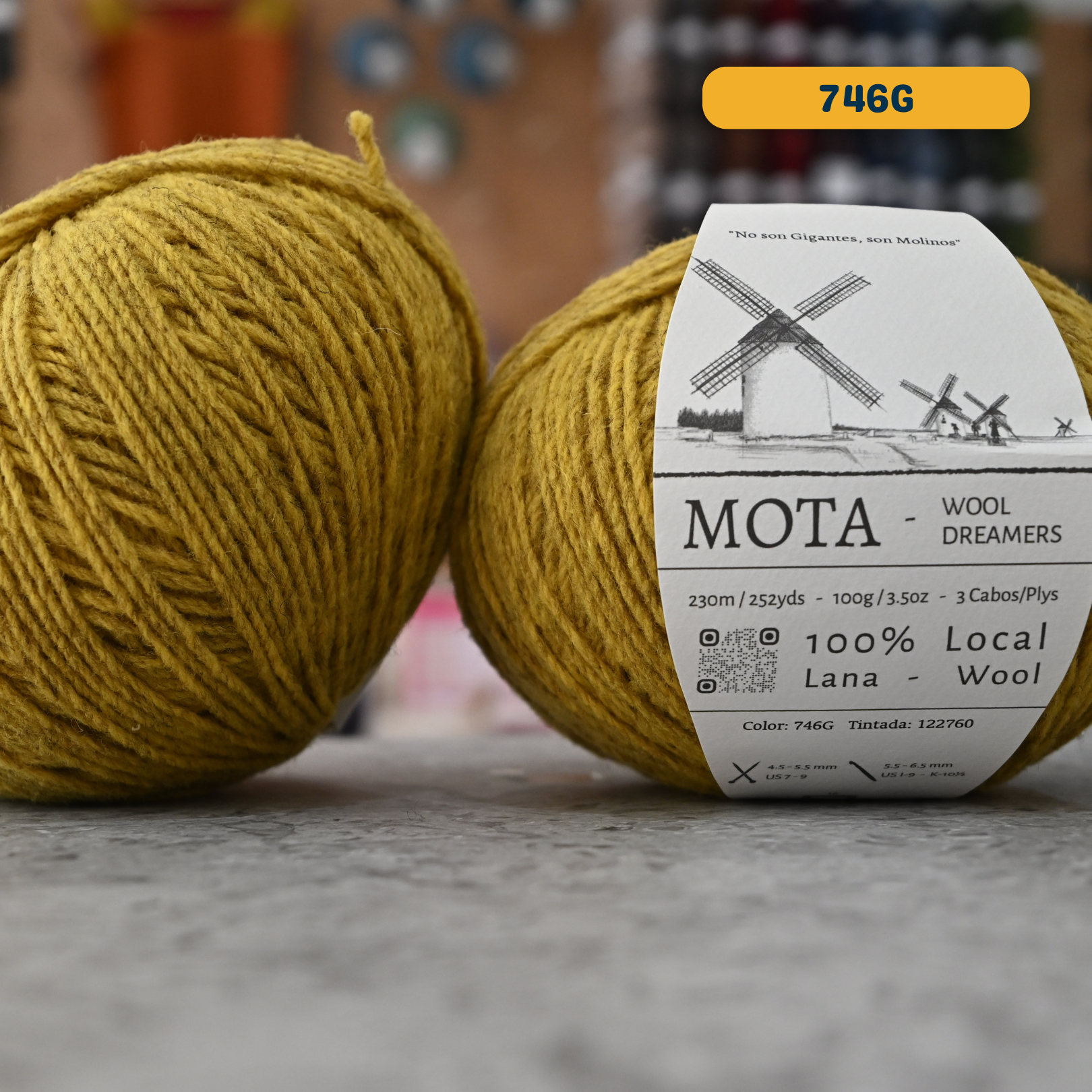 100g yellow (746G) merino & manchega wool yarn, 'Mota Wooldreamers 100% Wool' label visible, craft shop background (blurred)
