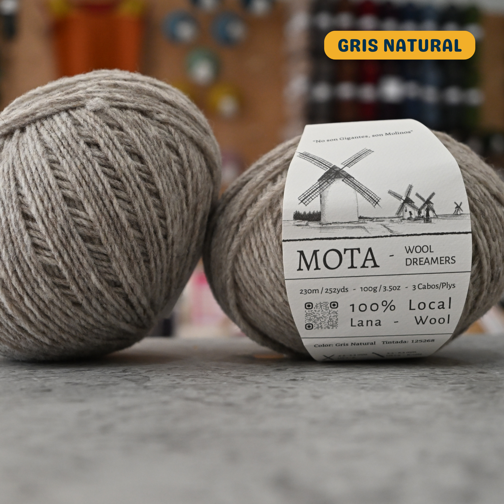 100g natural grey (gris natural)  merino & manchega wool yarn, 'Mota Wooldreamers 100% Wool' label visible, craft shop background (blurred)