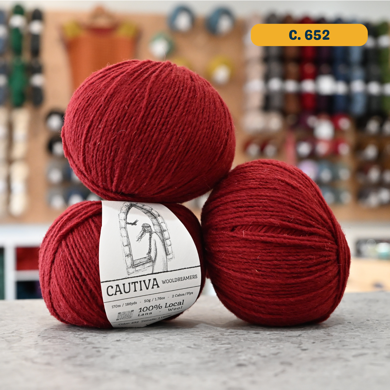 50g red (c. 652) merino & manchega wool sport yarn, 'Cautiva Wooldreamers  100% Wool' label visible, craft shop background (blurred)