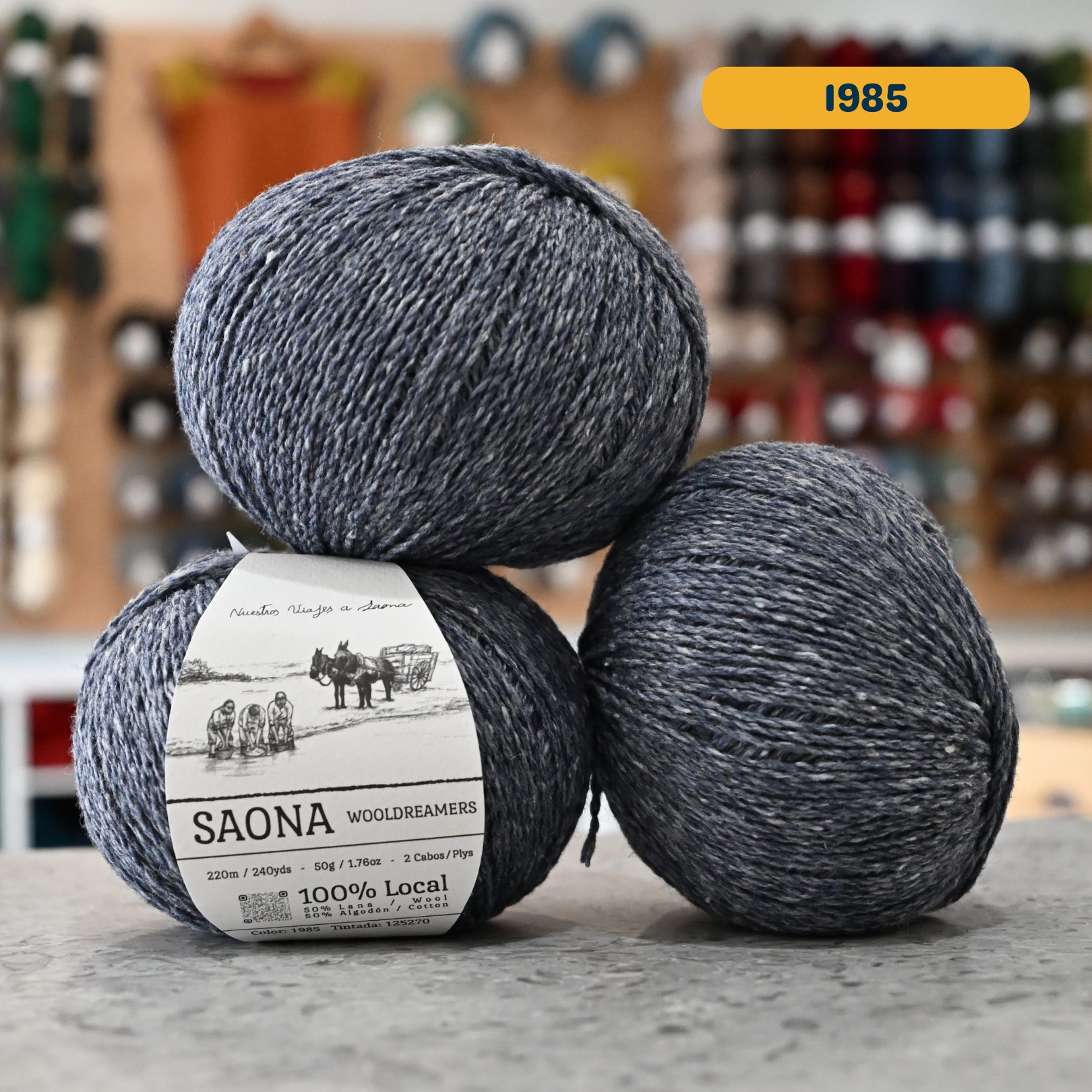 50g dark grey-blue (1985) wool & cotton fingering yarn, 'Saona Wooldreamers' label visible, craft shop background (blurred)
