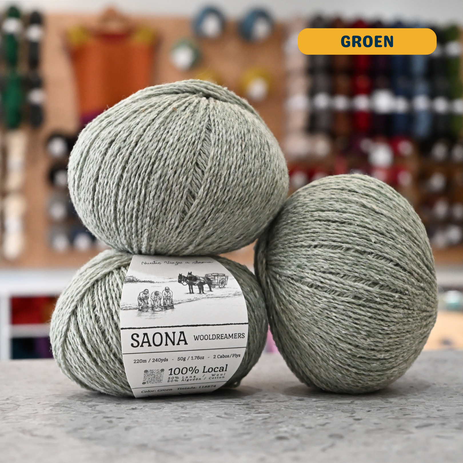 50g light green (groen) wool & cotton fingering yarn, 'Saona Wooldreamers' label visible, craft shop background (blurred)
