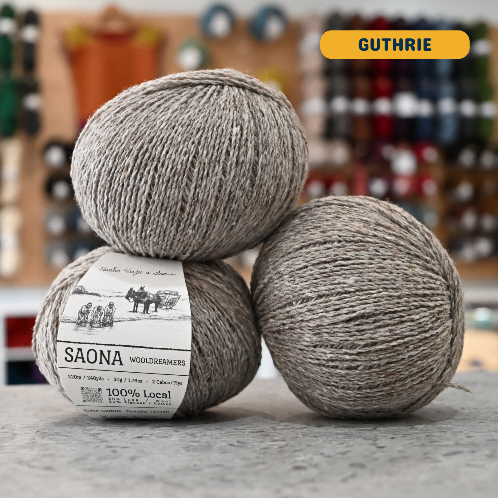50g light grey-beige (guthrie) wool & cotton fingering yarn, 'Saona Wooldreamers' label visible, craft shop background (blurred)
