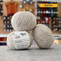 50g light beige (ozatta) wool & cotton fingering yarn, 'Saona Wooldreamers' label visible, craft shop background (blurred)