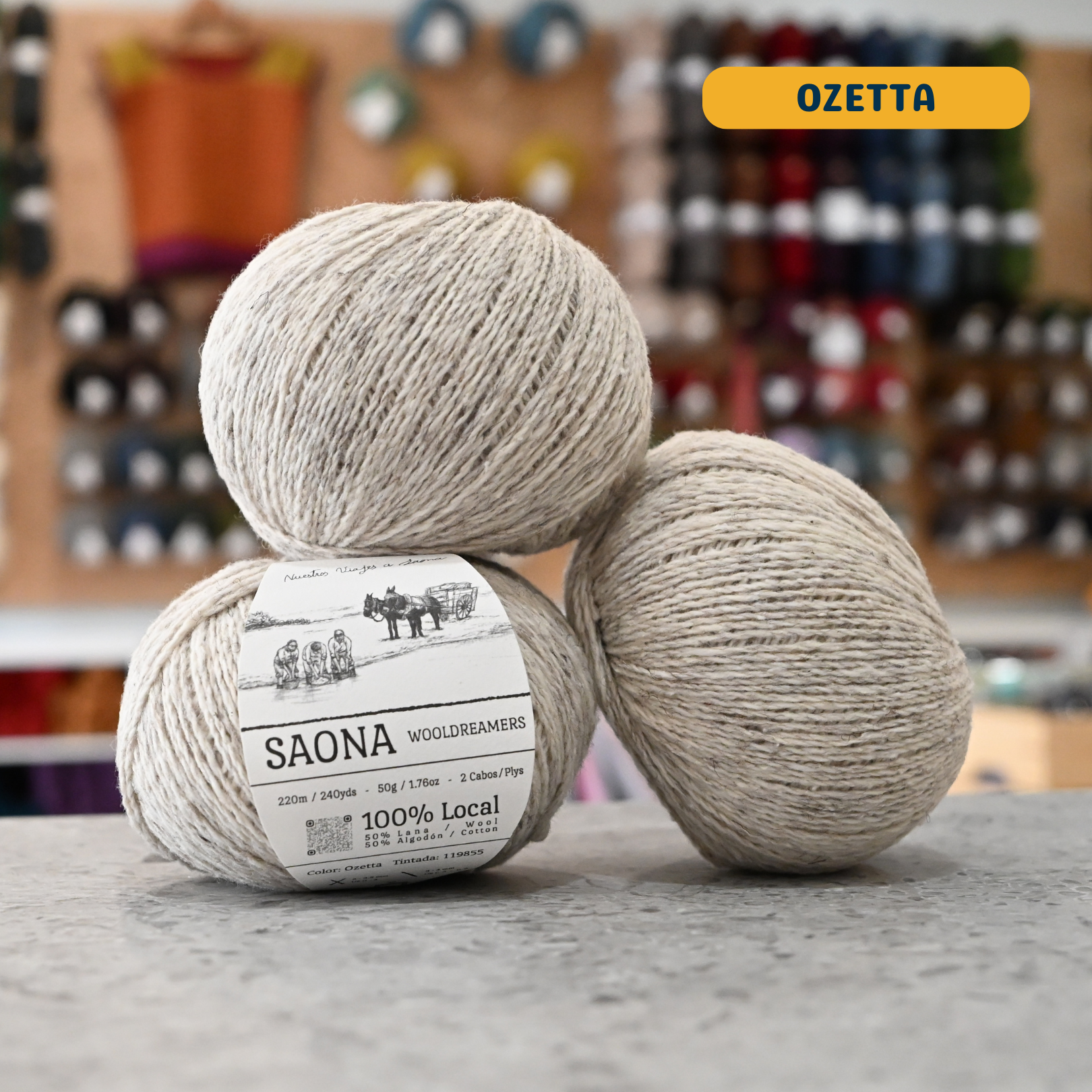 50g light beige (ozatta) wool & cotton fingering yarn, 'Saona Wooldreamers' label visible, craft shop background (blurred)