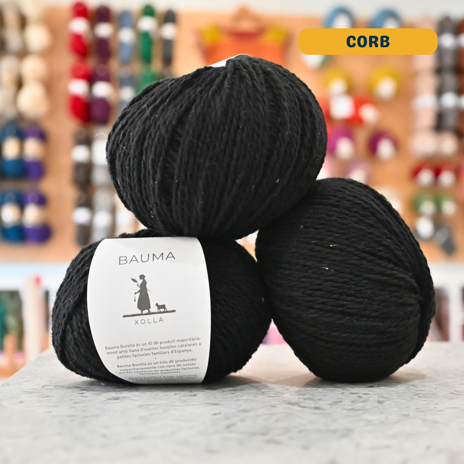 50g black (corb) Spanish wool DK yarn, 'Bauma Xolla' label visible, craft shop background (blurred)