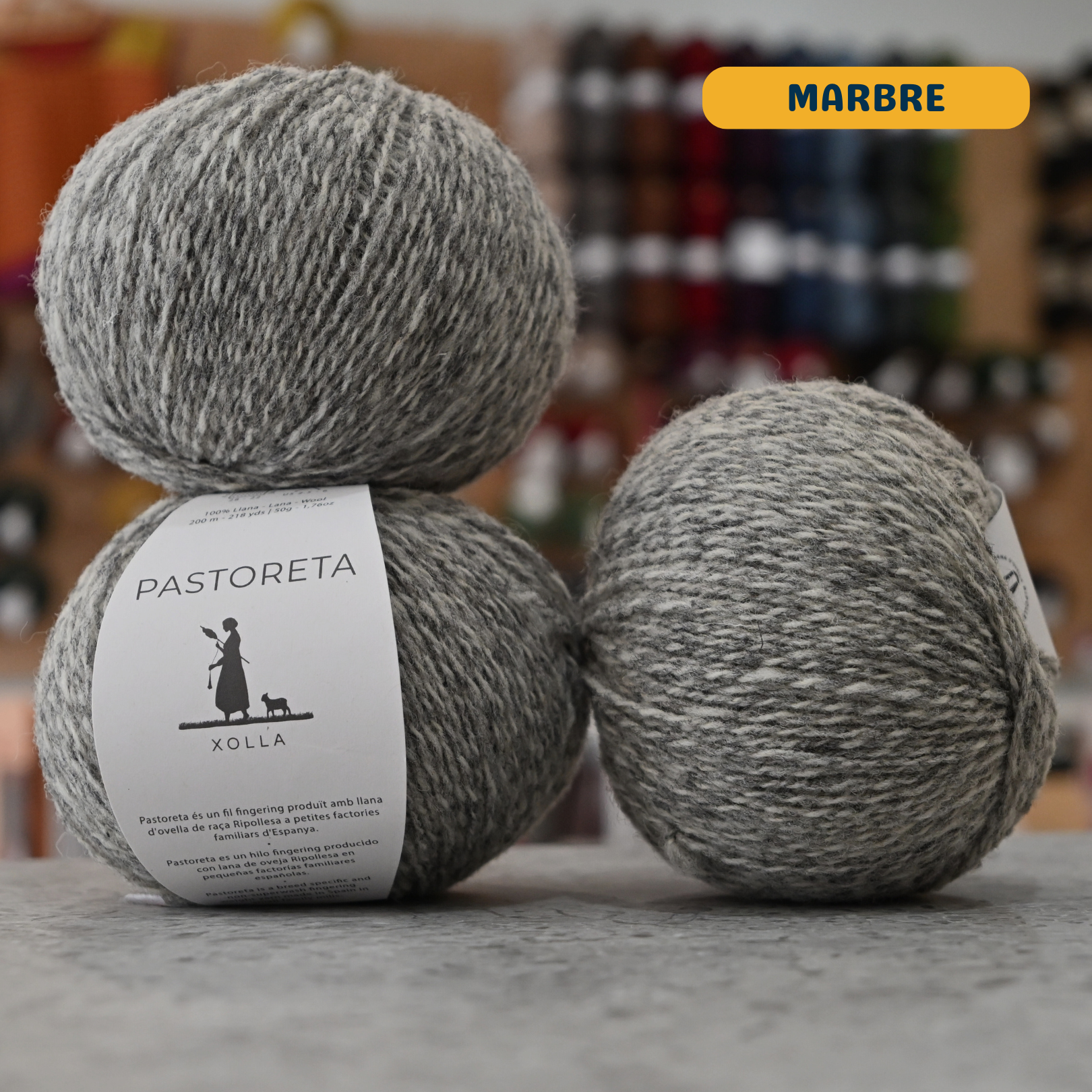 50g light grey and white marbled (marbre) Spanish wool fingering yarn, 'Pastoreta Xolla' label visible, craft shop background (blurred)
