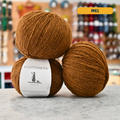 50g orange-brown (mel) Spanish wool fingering yarn, 'Pastoreta Xolla' label visible, craft shop background (blurred)
