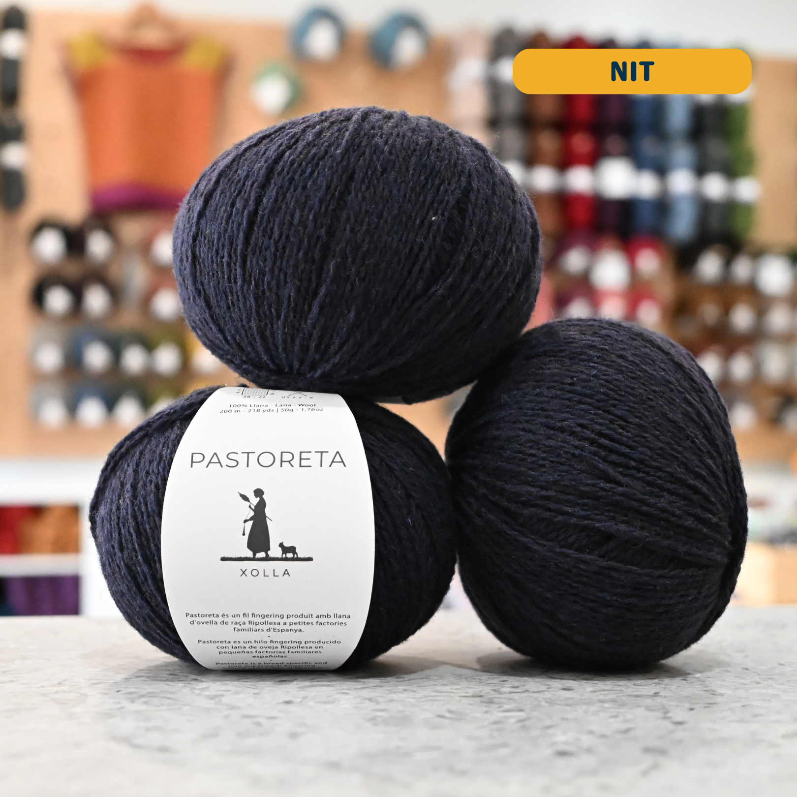 50g navy blue (nit) Spanish wool fingering yarn, 'Pastoreta Xolla' label visible, craft shop background (blurred)
