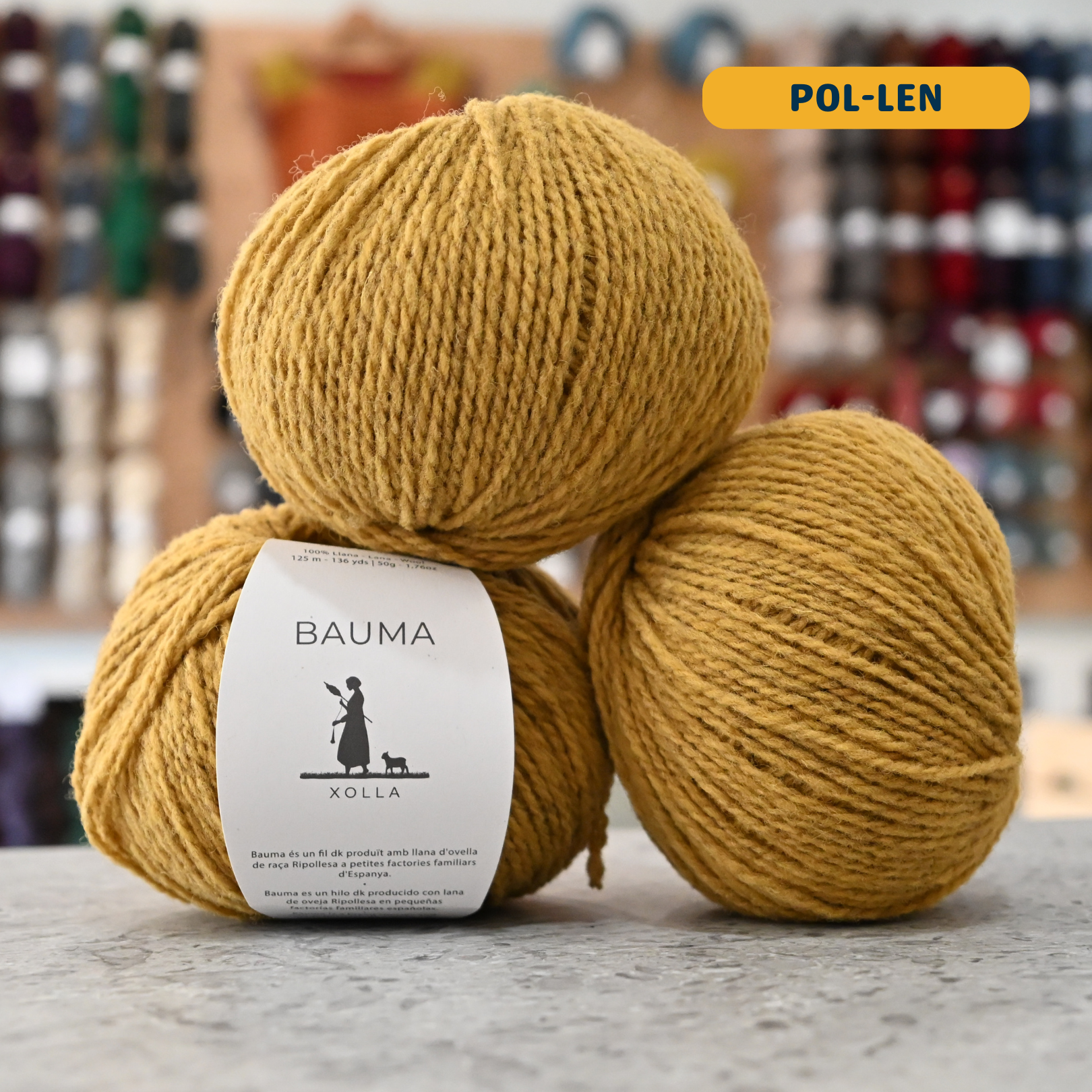 50g yellow (pol-len) Spanish wool DK yarn, 'Bauma Xolla' label visible, craft shop background (blurred)