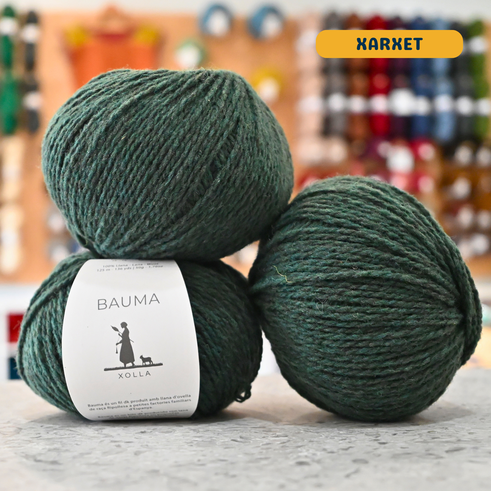 50g dark turquoise (xarxet) Spanish wool DK yarn, 'Bauma Xolla' label visible, craft shop background (blurred)
