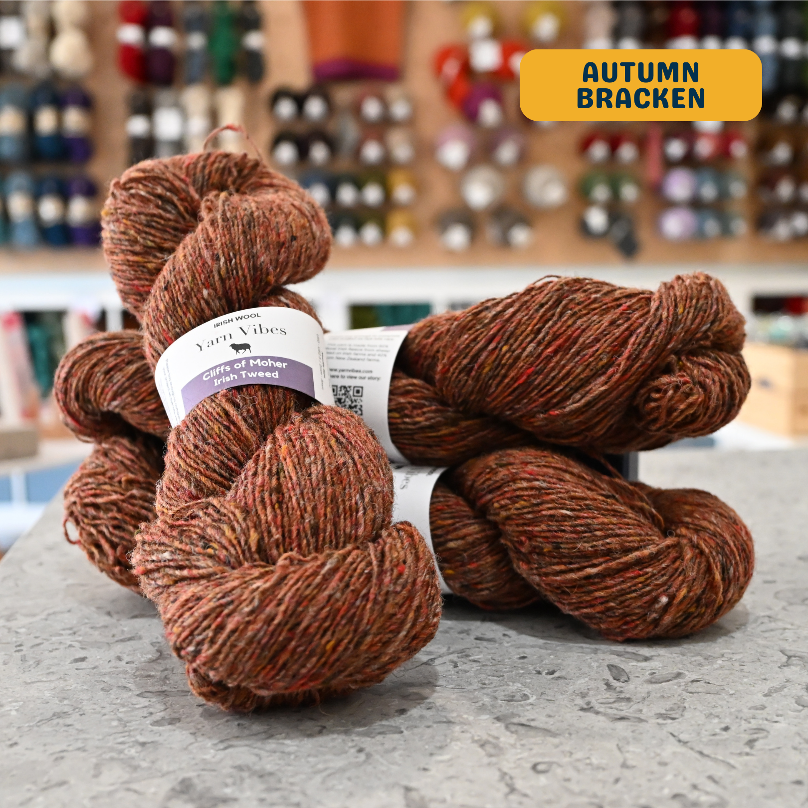 100g brown-orange tweed (autumn bracken) Irish wool merino sport yarn, 'Yarn Vibes Cliffs of Moher Irish Tweed' label visible, craft shop background (blurred)