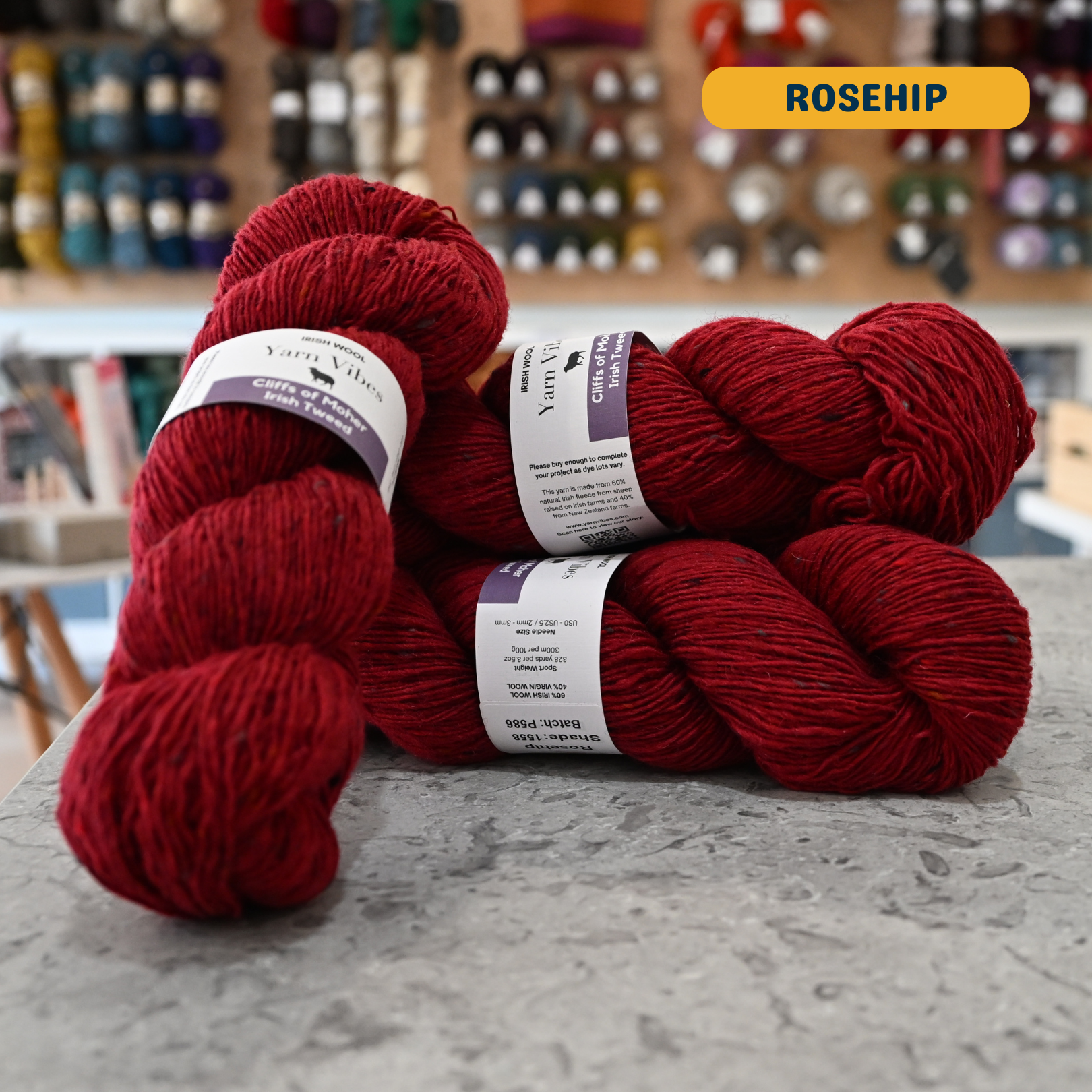 100g red (rosehip) Irish wool merino sport yarn, 'Yarn Vibes Cliffs of Moher Irish Tweed' label visible, craft shop background (blurred)