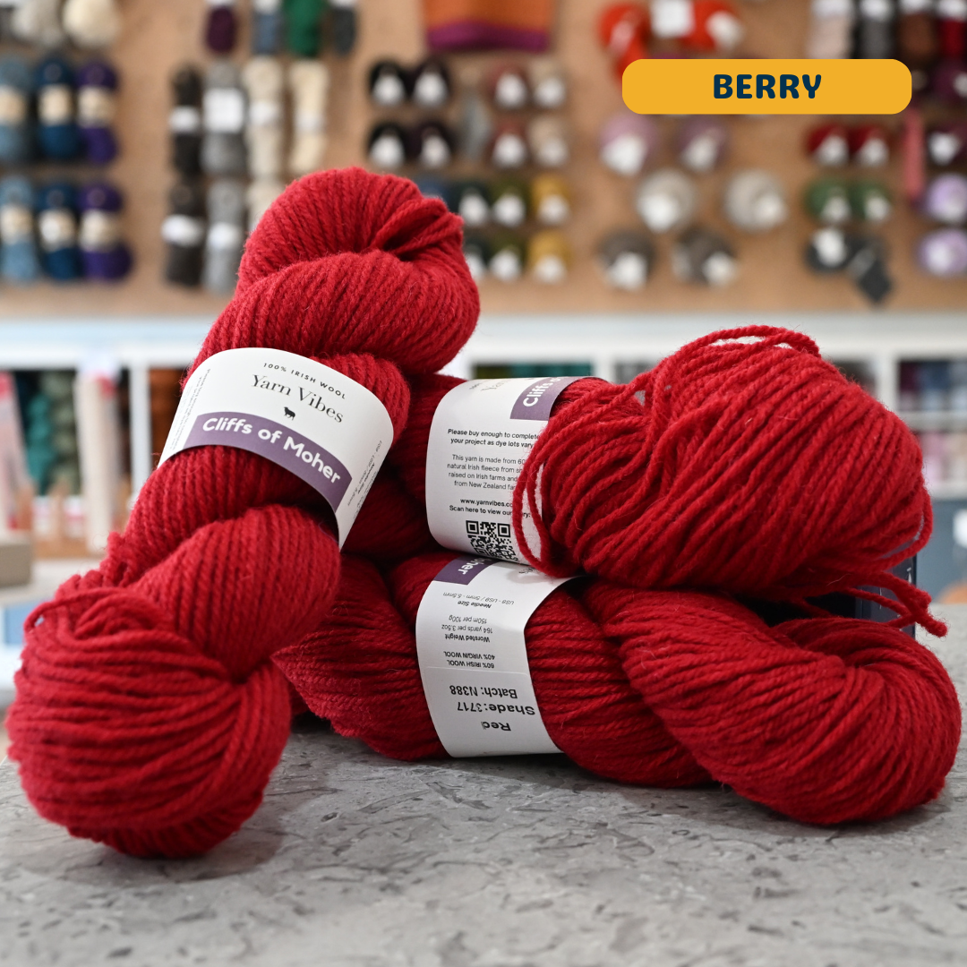 100g red (berry) Irish wool  merino aran yarn, 'Yarn Vibes Cliffs of Moher' label visible, craft shop background (blurred)