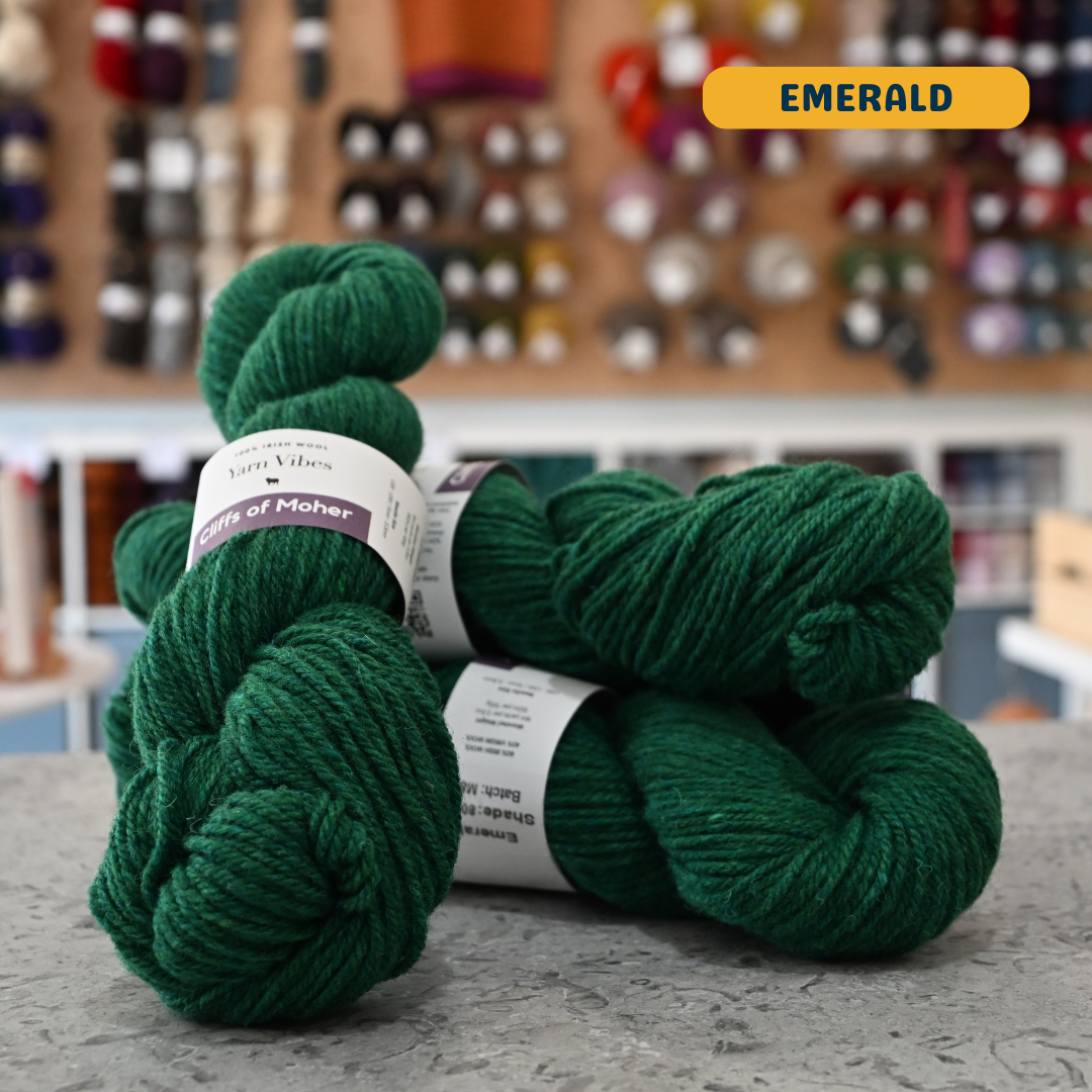 100g emerald green Irish wool  merino aran yarn, 'Yarn Vibes Cliffs of Moher' label visible, craft shop background (blurred)