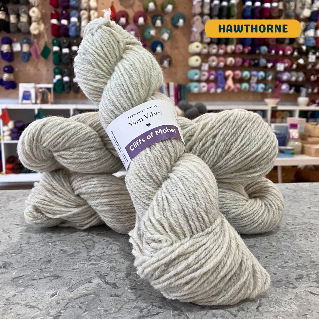 100g heathered beige (hawthorne) Irish wool  merino aran yarn, 'Yarn Vibes Cliffs of Moher' label visible, craft shop background (blurred)