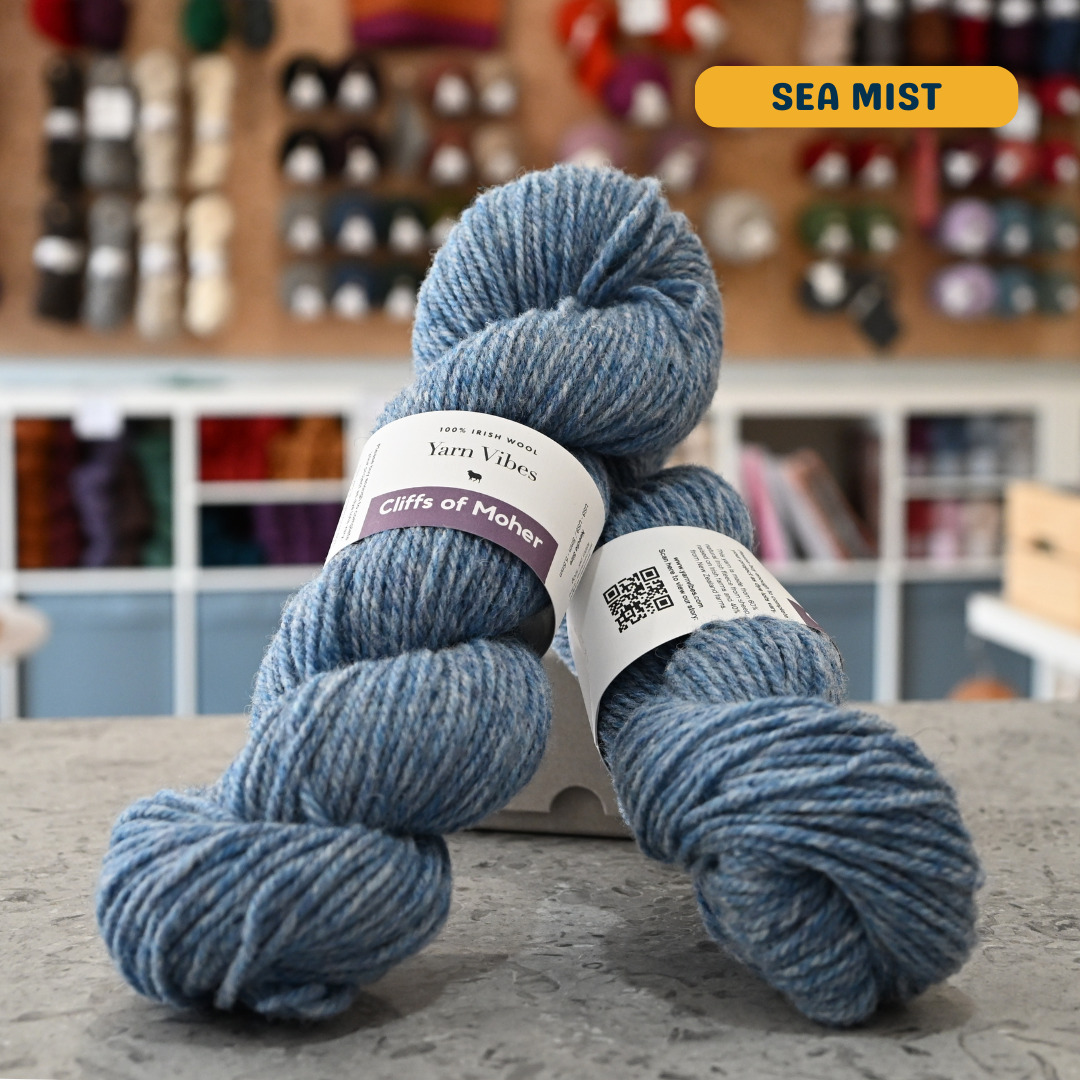 100g light blue (sea mist) Irish wool  merino aran yarn, 'Yarn Vibes Cliffs of Moher' label visible, craft shop background (blurred)