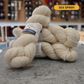 100g natural white (sea spray) Irish wool  merino aran yarn, 'Yarn Vibes Cliffs of Moher' label visible, craft shop background (blurred)