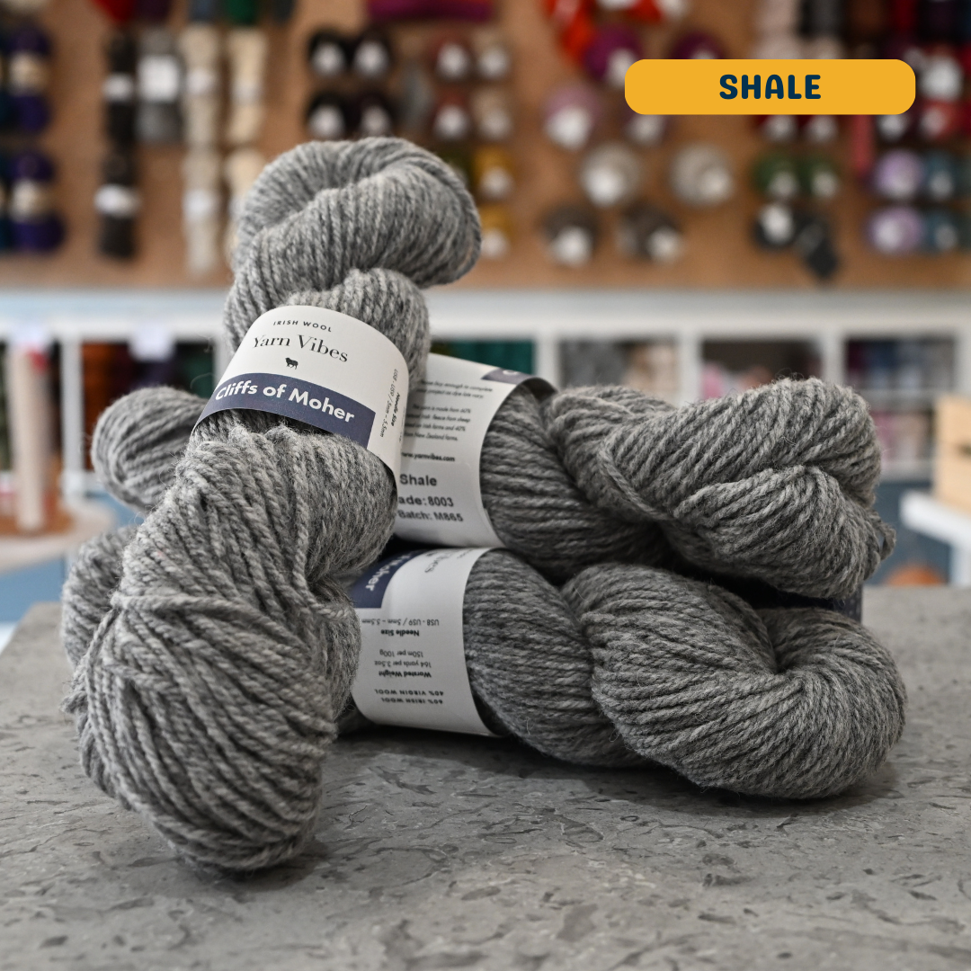 100g grey (shale) Irish wool  merino aran yarn, 'Yarn Vibes Cliffs of Moher' label visible, craft shop background (blurred)
